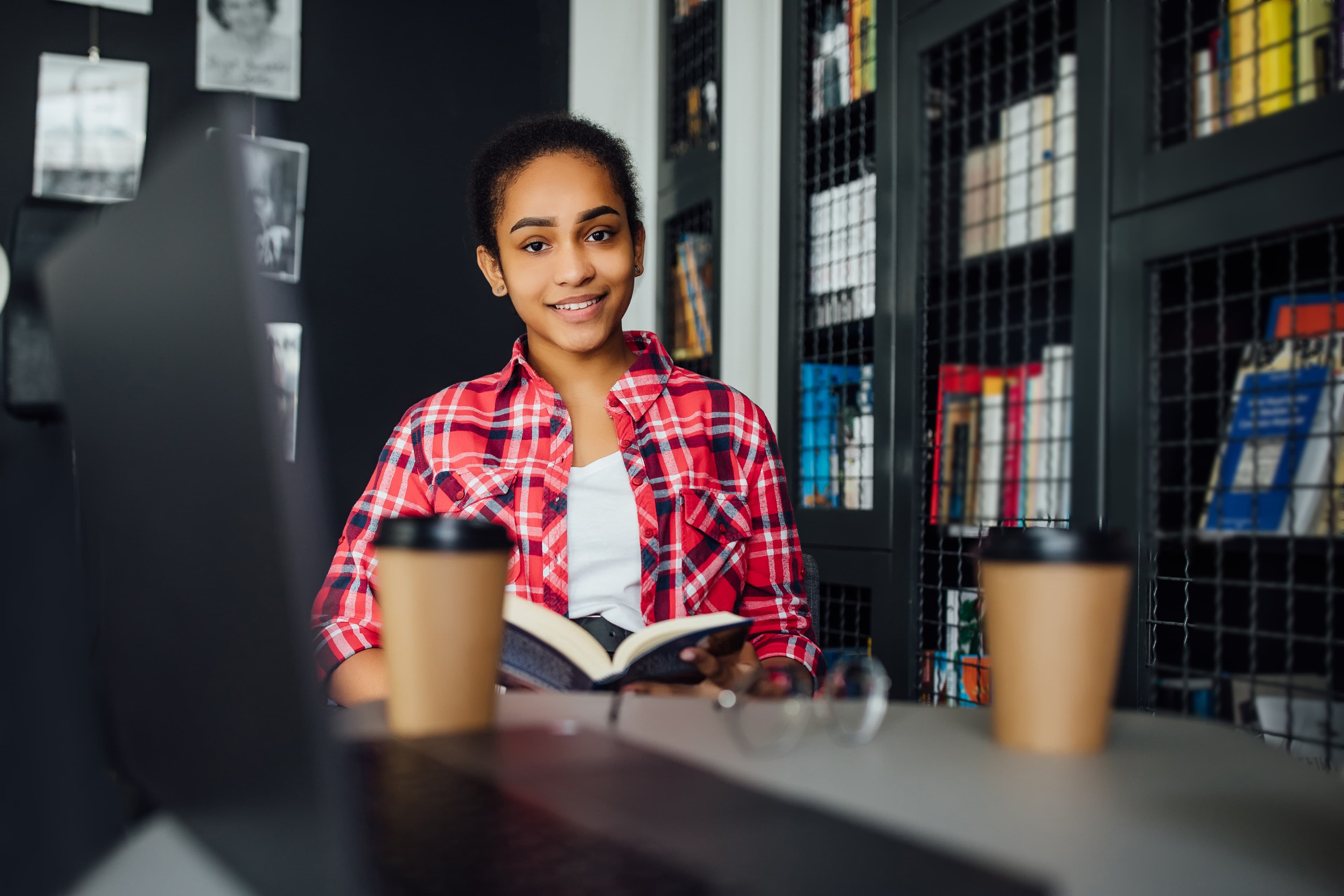 Young woman smiling at a desk with an open book and two coffee cups