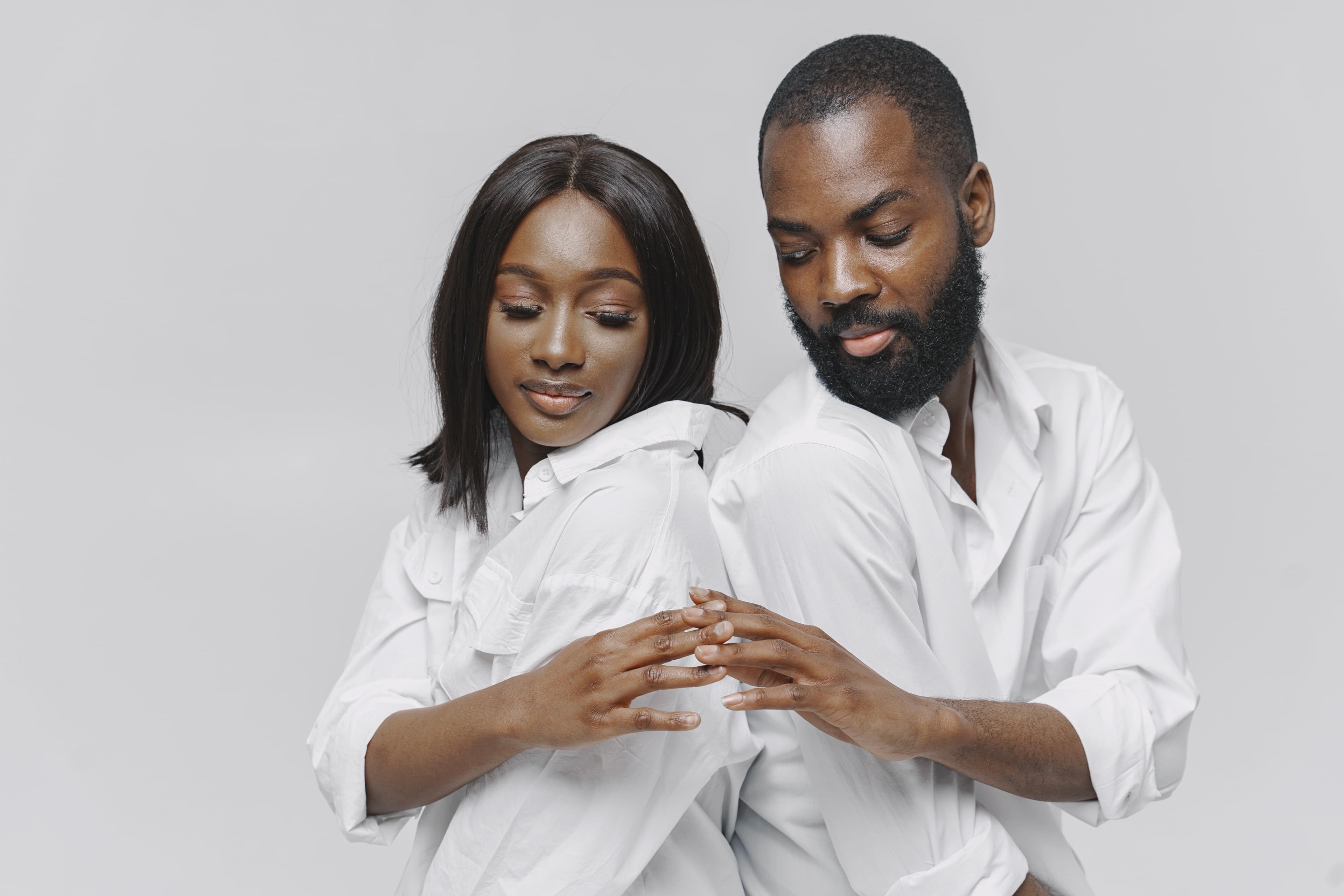 Couple in white shirts standing back to back, their hands almost touching