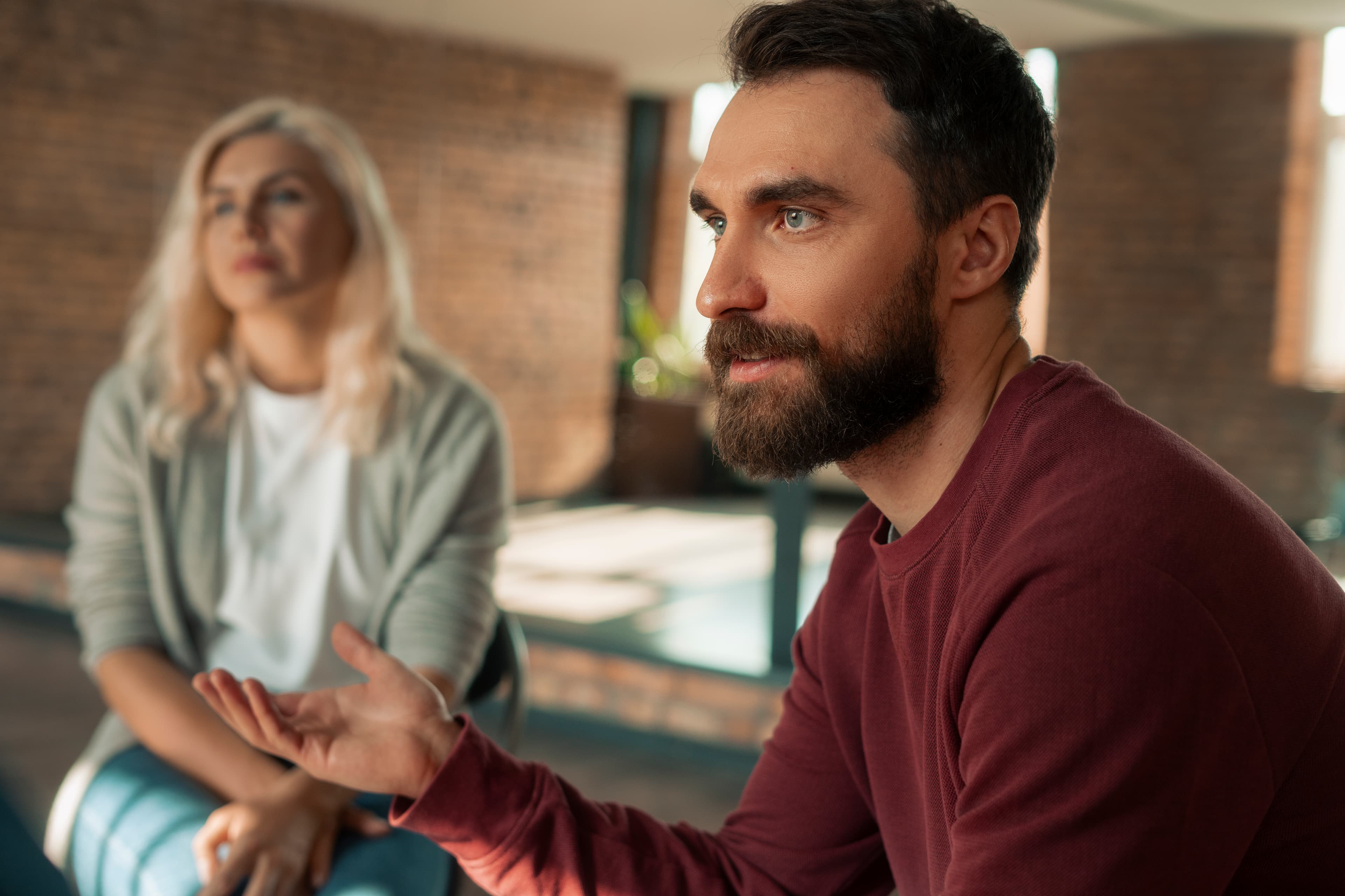 Bearded man speaking, a woman blurred beside him
