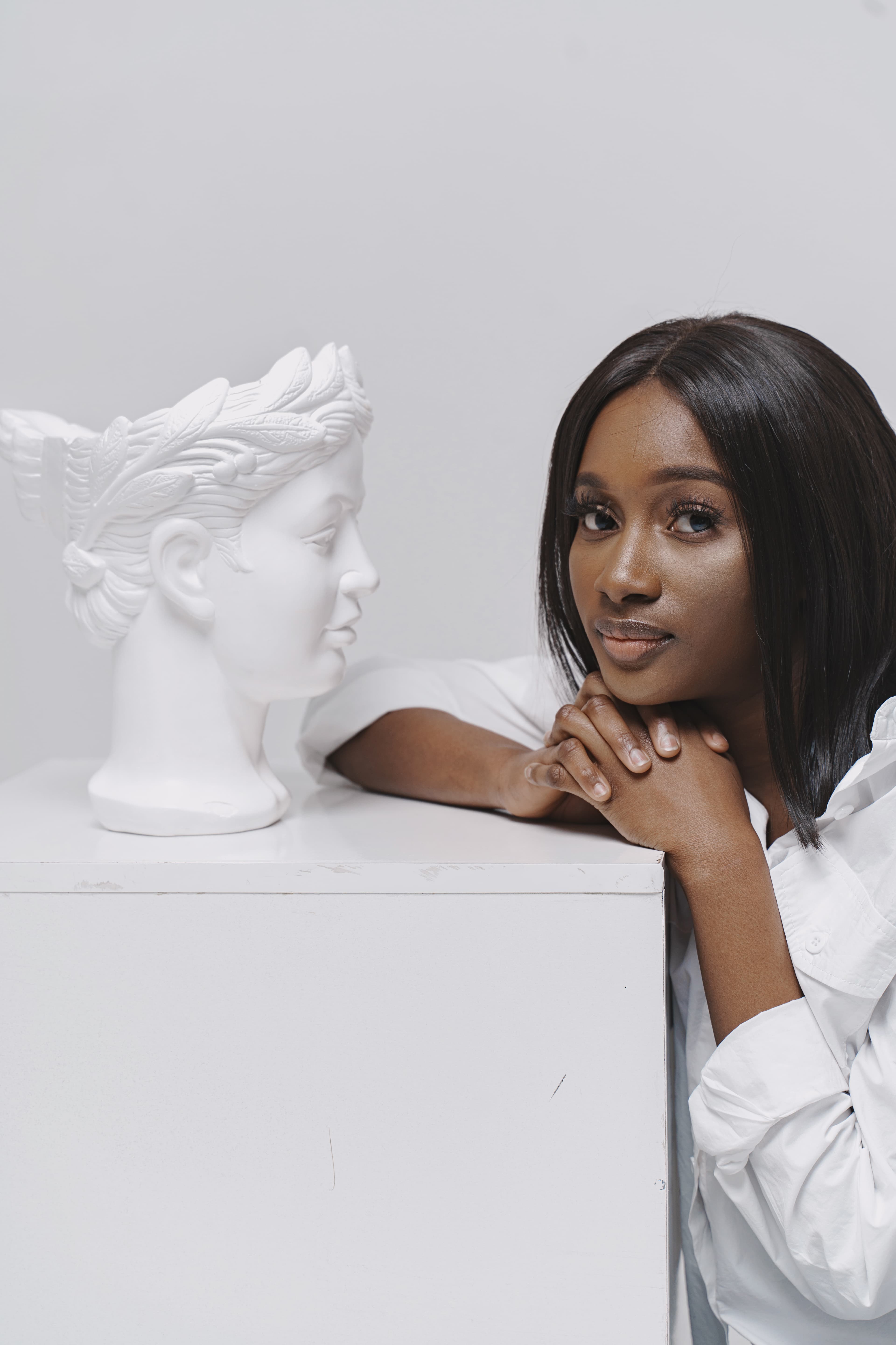 Woman resting her chin on her hands beside a white sculpted bust