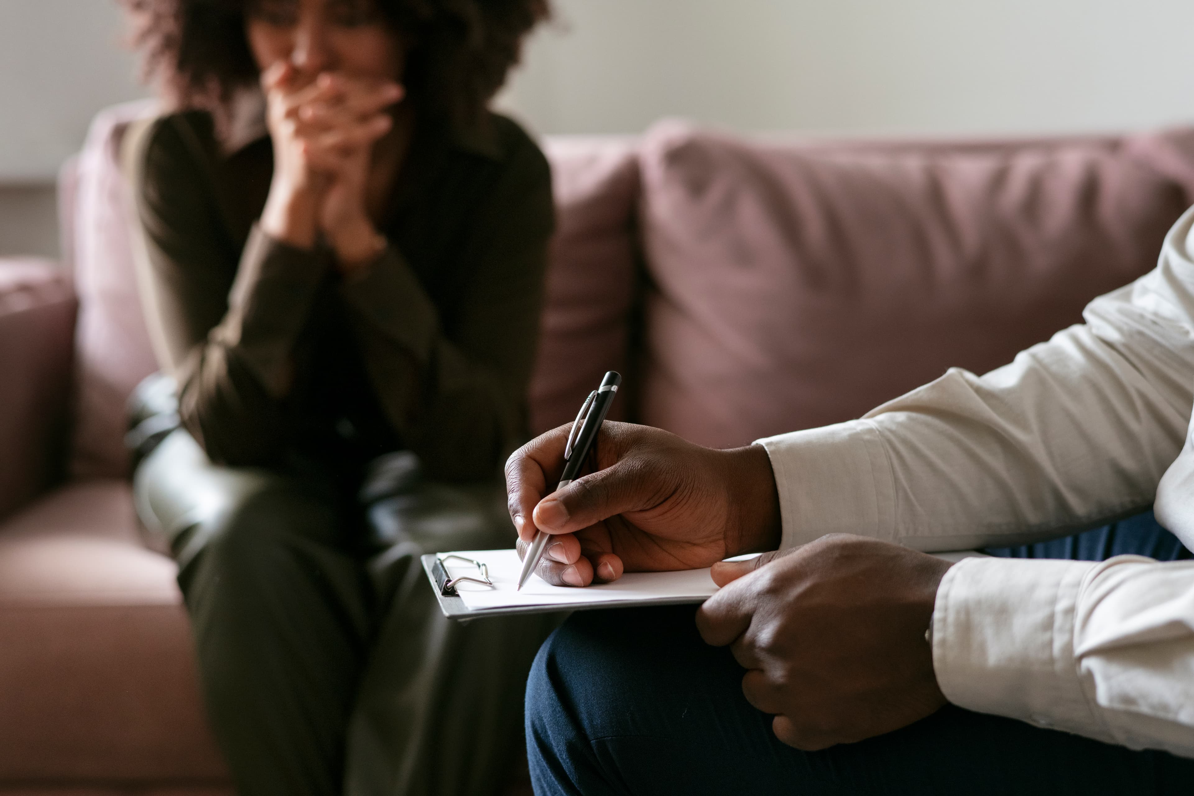 Counsellor taking notes while a client sits on a sofa