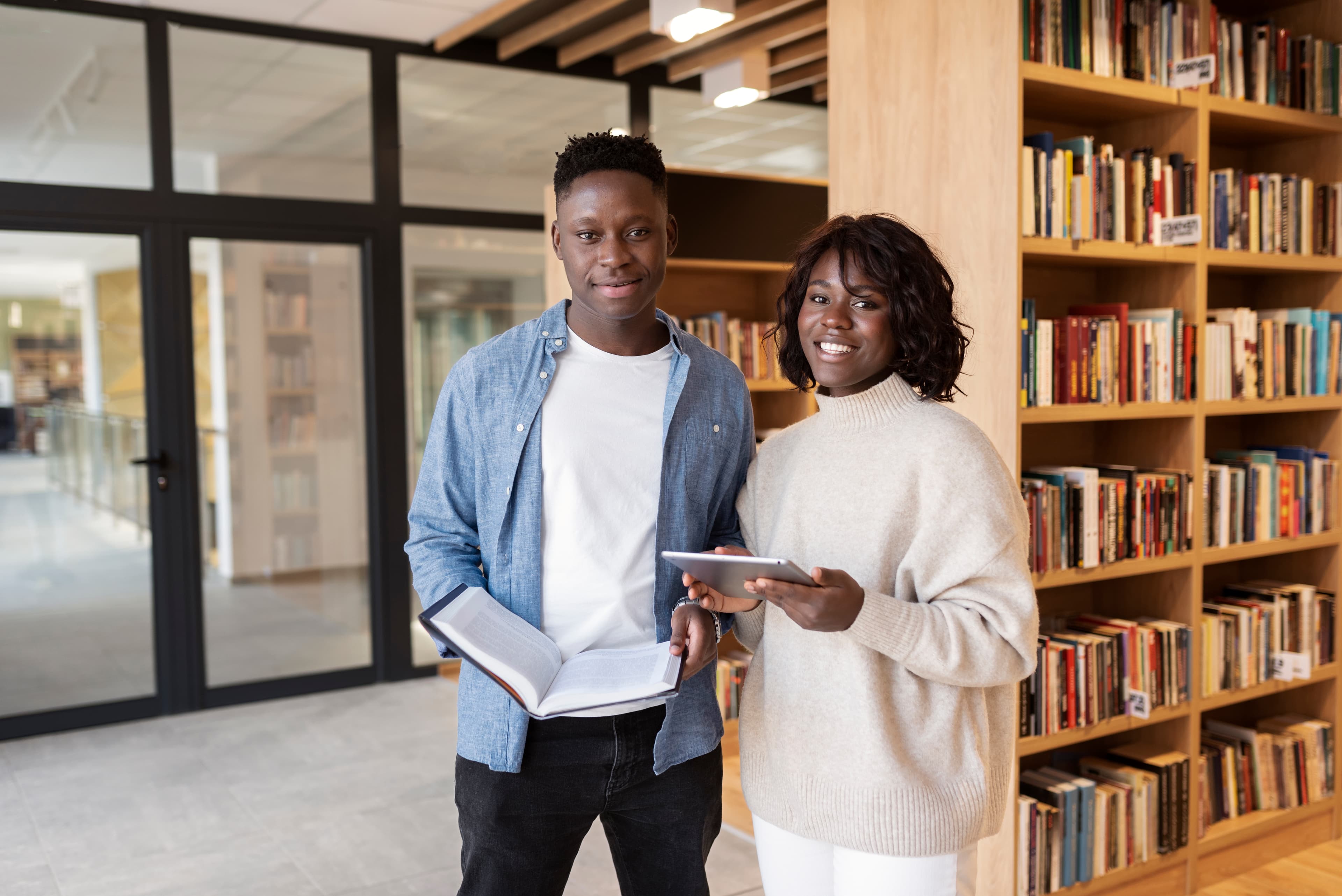 Couple standing in a library, holding a book and a tablet