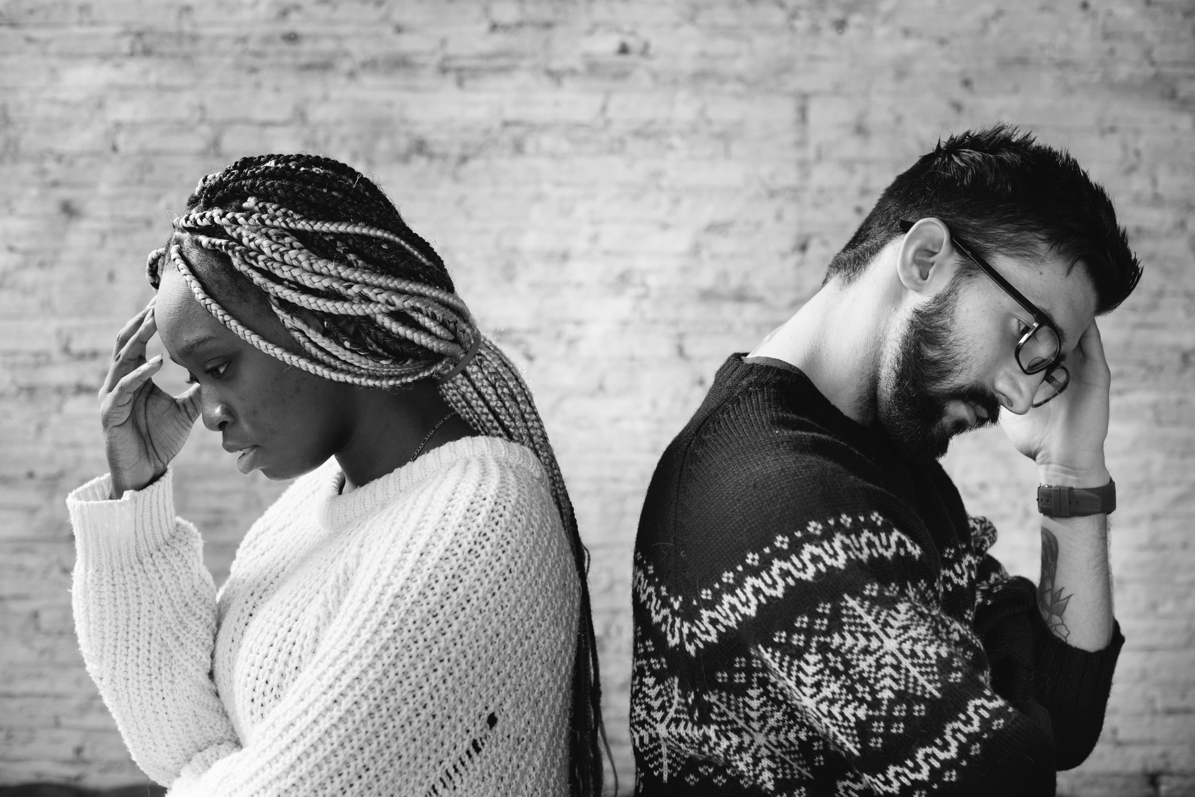 Black and white photo of a couple sitting back to back, heads lowered